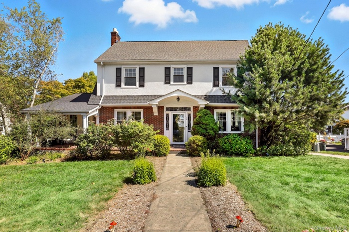 View of front of home with a front lawn, a chimney, a shingled roof, and brick siding