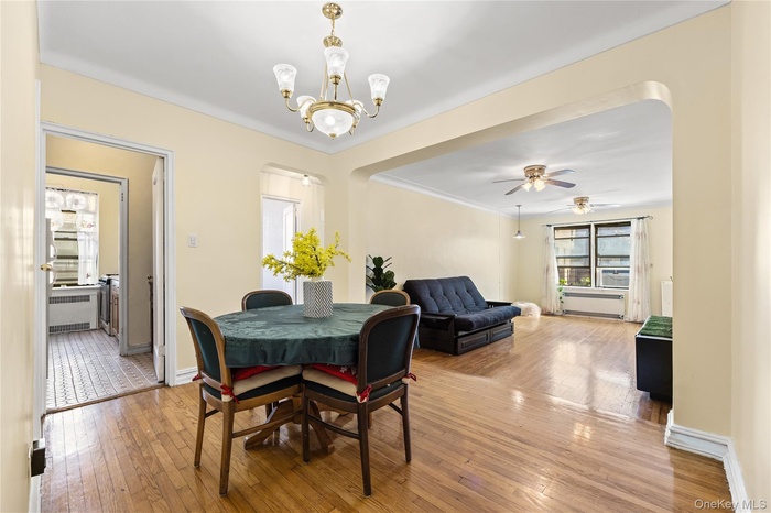 Dining room featuring light wood-style floors, radiator heating unit, crown molding, ceiling fan, and a chandelier