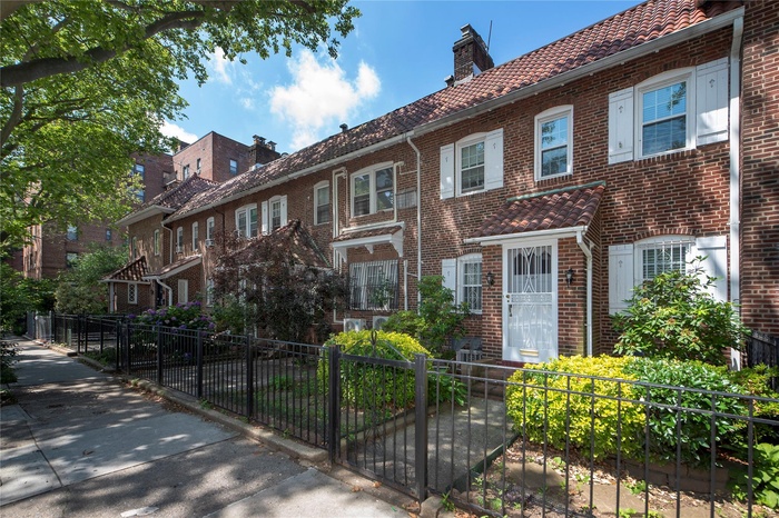 Townhome / multi-family property featuring a fenced front yard, brick siding, a tile roof, and a chimney