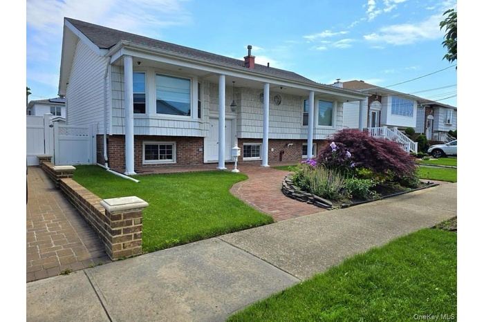 Raised ranch featuring brick siding, a front lawn, a chimney, a gate, and a porch
