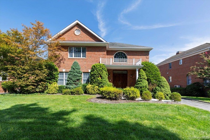 View of front of property featuring a balcony, brick siding, and a front lawn