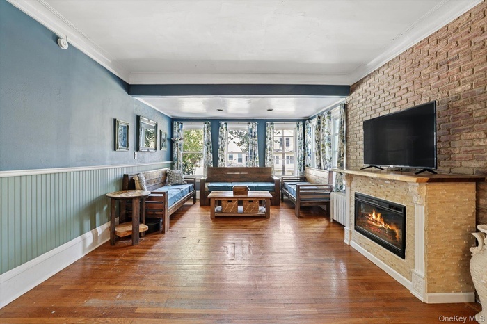 Living room with hardwood / wood-style flooring, crown molding, wainscoting, and a large fireplace