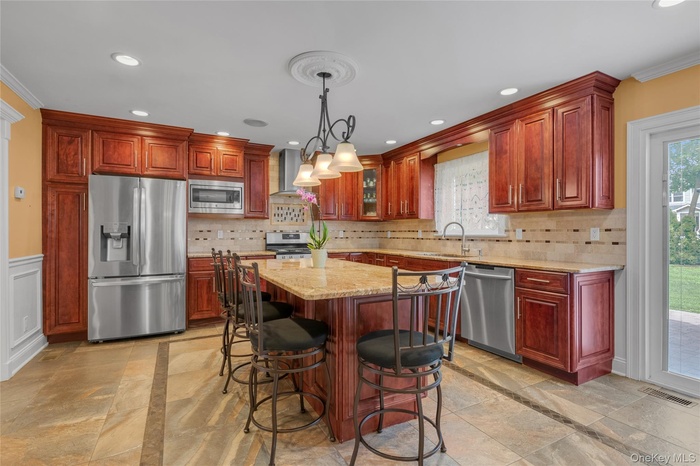 Kitchen with appliances with stainless steel finishes, light stone counters, healthy amount of natural light, pendant lighting, and ornamental molding