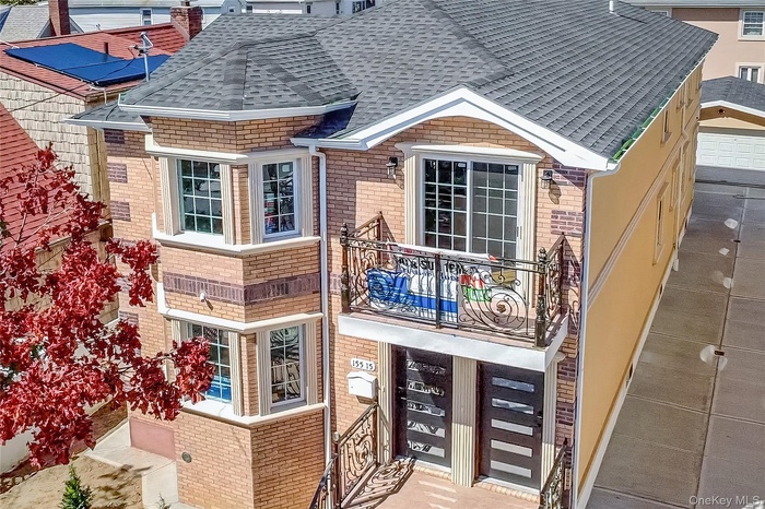 Rear view of property with brick siding, roof with shingles, and a balcony