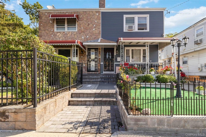 View of front of property with a fenced front yard, a gate, a chimney, and stone siding
