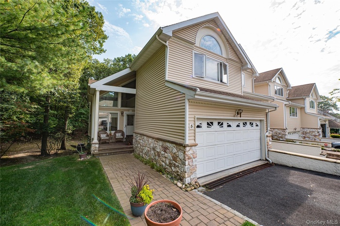 View of front facade featuring an attached garage, stone siding, driveway, and a front lawn
