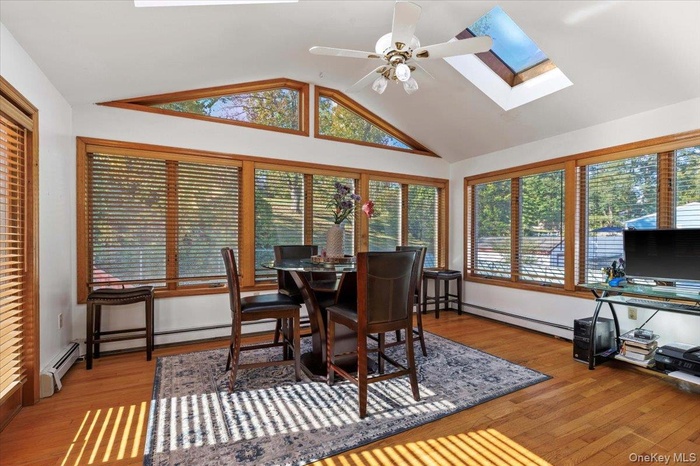 Sunroom featuring plenty of natural light, lofted ceiling, a skylight, and baseboard heating