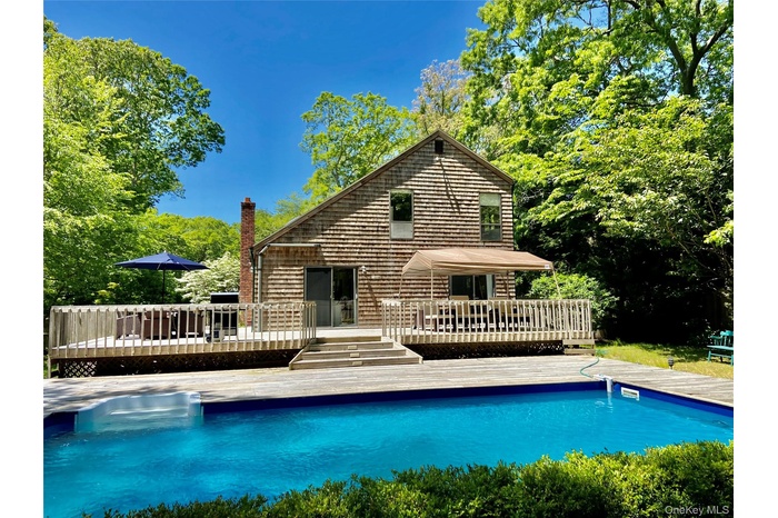 Back of house featuring a deck, an outdoor pool, and view of wooded area