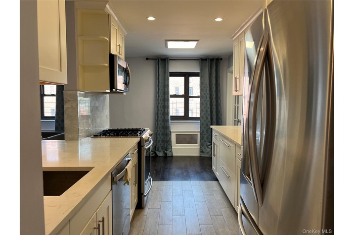 Kitchen featuring stainless steel appliances, white cabinetry, dark wood-style flooring, light stone counters, and recessed lighting