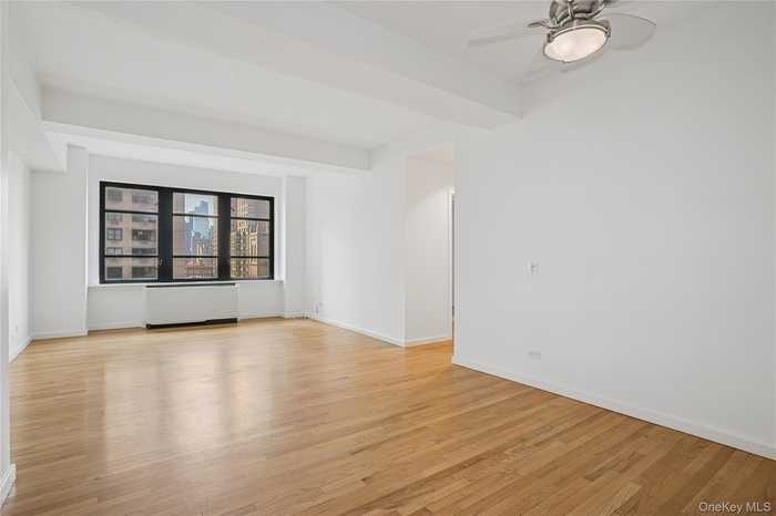 Spare room featuring light wood-style flooring, beam ceiling, radiator heating unit, and a ceiling fan