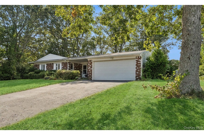 Ranch-style home featuring brick siding, asphalt driveway, a front lawn, an attached garage, and view of wooded area