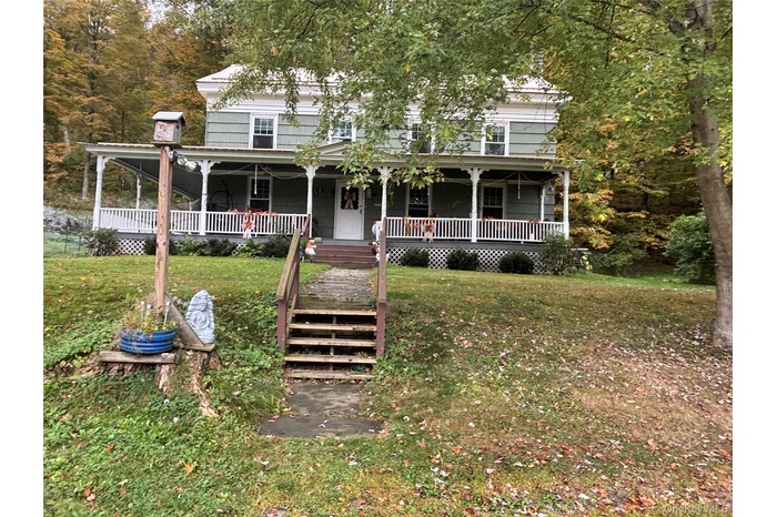 View of front of home with a front yard, a porch, stairway, and a chimney