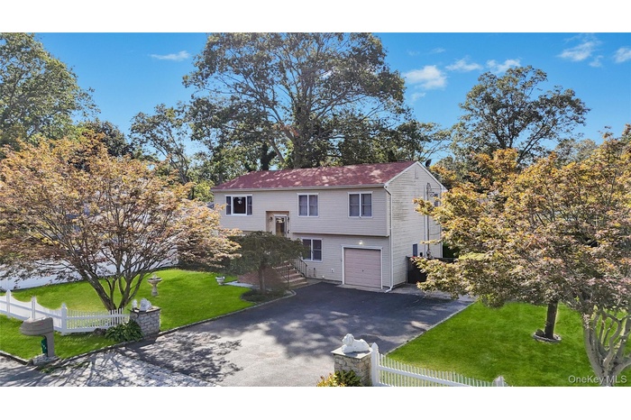 Split foyer home featuring driveway, a fenced front yard, and an attached garage