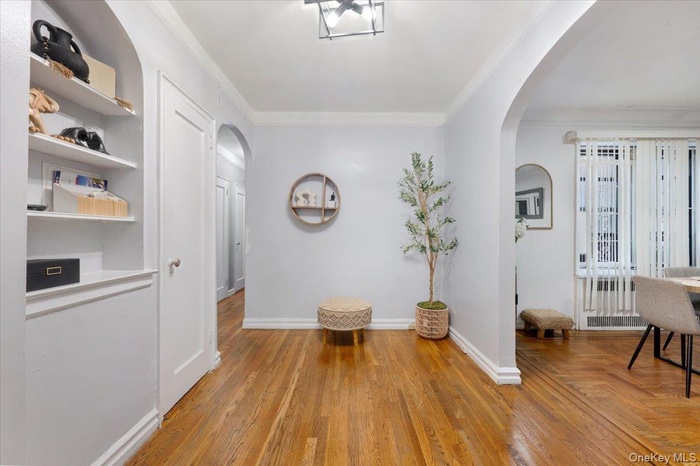 Corridor featuring light wood finished floors, ornamental molding, arched walkways, and built in shelves