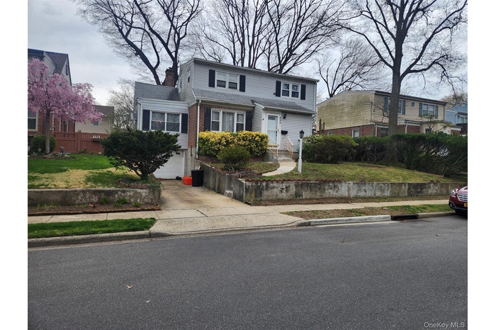 Traditional-style home featuring a front lawn, driveway, a chimney, and a garage