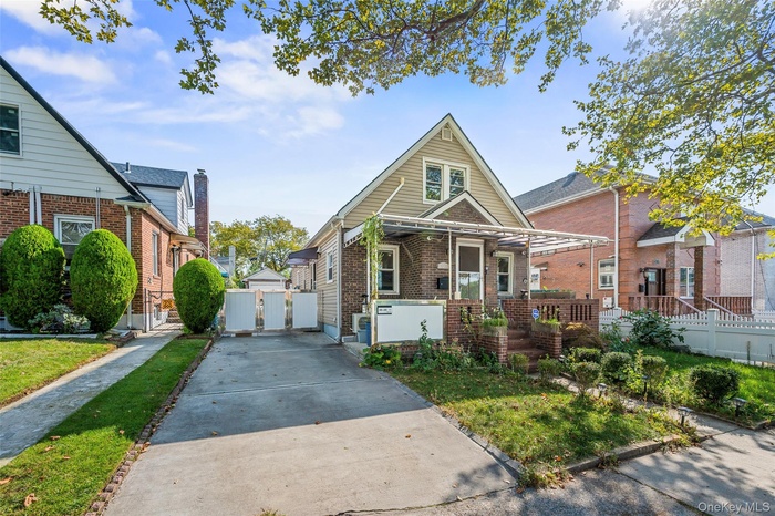 Bungalow-style house featuring brick siding, a gate, covered porch, concrete driveway, and a chimney
