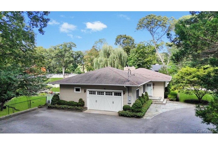 Ranch-style home with roof with shingles, an attached garage, view of wooded area, and asphalt driveway