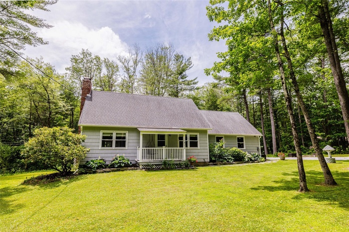 View of front of house featuring a chimney, a front yard, and a shingled roof