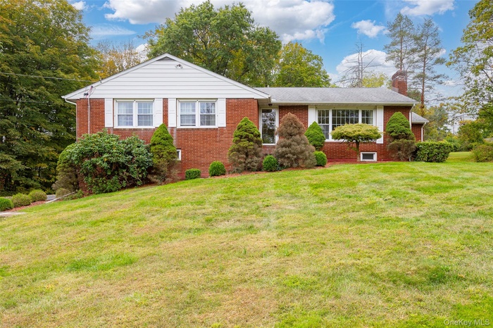 Ranch-style home featuring a chimney, brick siding, and a front yard