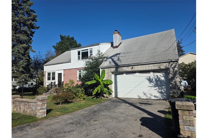 View of front facade with driveway, a chimney, brick siding, and a garage
