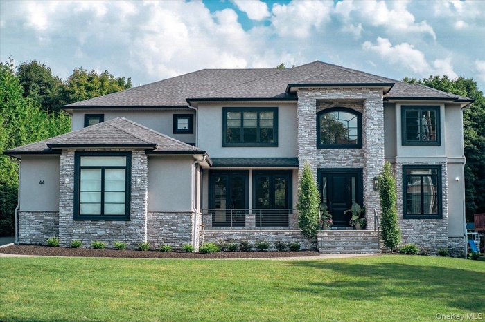 View of front facade featuring stucco siding, stone siding, a front yard, and roof with shingles