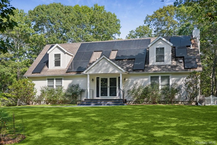 View of front of house with a chimney, a front yard, solar panels, and a shingled roof