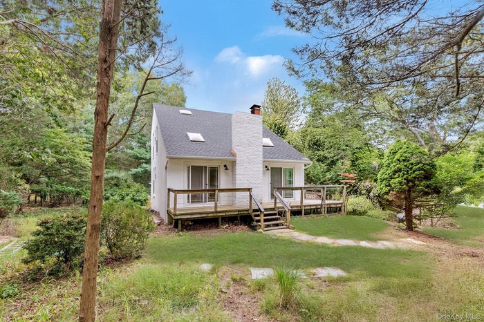Rear view of property with a chimney, a shingled roof, a lawn, and a deck