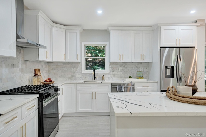 Kitchen featuring appliances with stainless steel finishes, wall chimney range hood, light stone countertops, and recessed lighting
