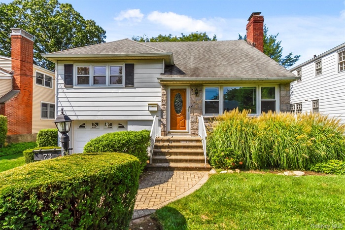 Tri-level home featuring an attached garage, a shingled roof, stone siding, a chimney, and a front lawn