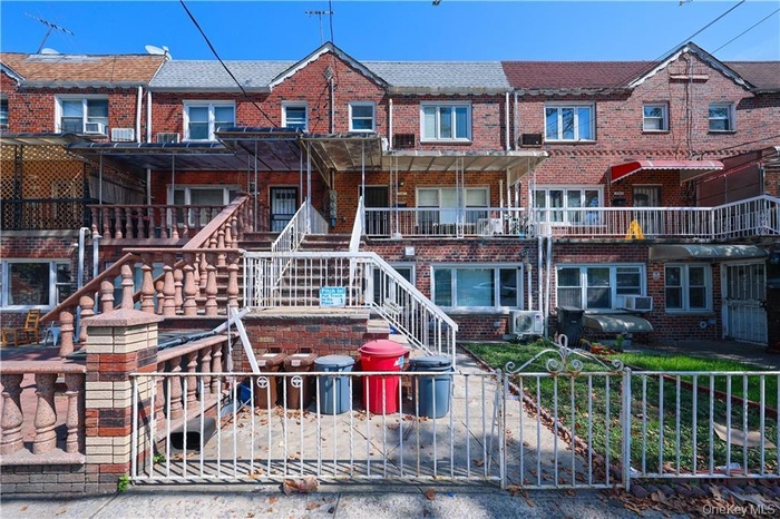 Traditional-style home with brick siding, a balcony, a fenced front yard, stairs, and a gate