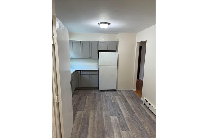 Kitchen featuring gray cabinets, freestanding refrigerator, dark wood-style flooring, and a baseboard heating unit