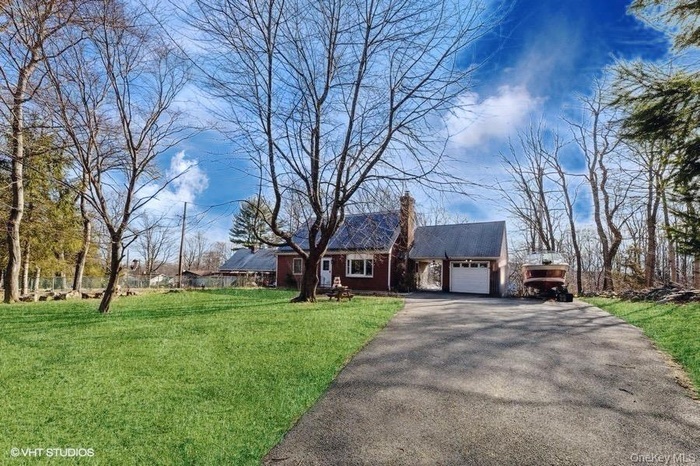 View of front of home featuring driveway, a front yard, a chimney, and an attached garage