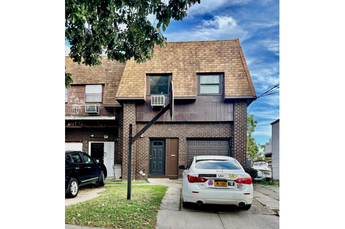 View of front facade with brick siding, driveway, a shingled roof, an attached garage, and a wall unit AC