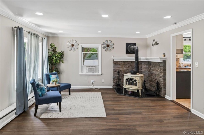 Living area with a wood stove, ornamental molding, wood finished floors, recessed lighting, and a baseboard radiator