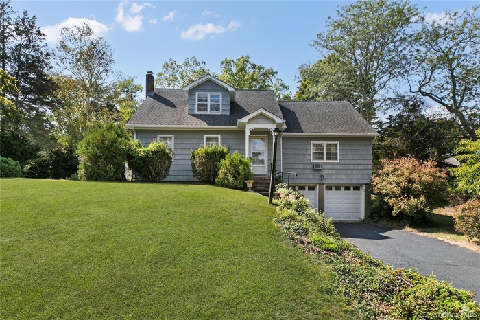 New england style home with a chimney, a front yard, a shingled roof, asphalt driveway, and an attached garage