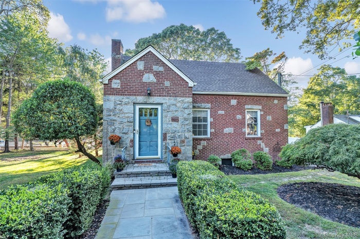 View of front facade featuring a chimney, a front yard, brick siding, and stone siding