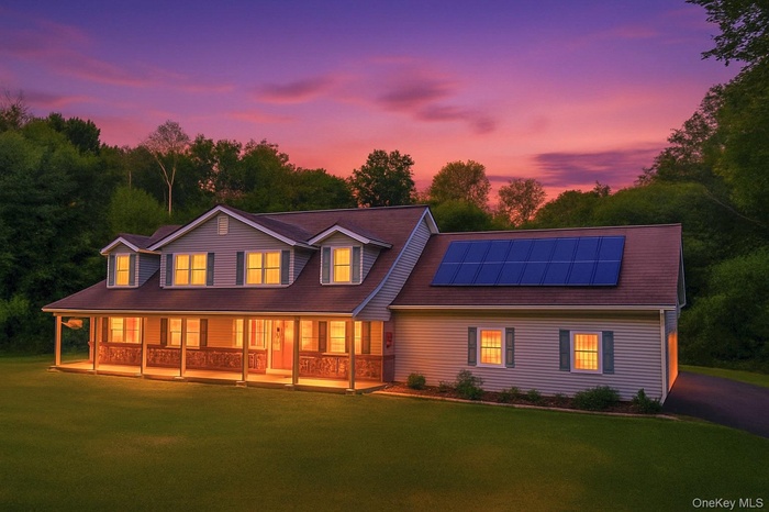 View of front of home with covered porch, solar panels, and a yard