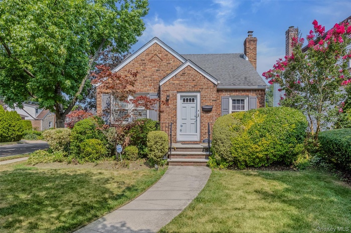 View of front of house featuring a chimney, a front lawn, roof with shingles, and brick siding