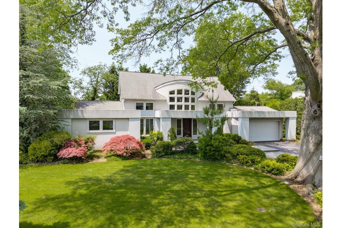 Art deco house featuring a front yard, stucco siding, a garage, and roof with shingles