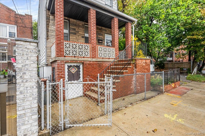 Doorway to property featuring a gate, brick siding, covered porch, and stone siding