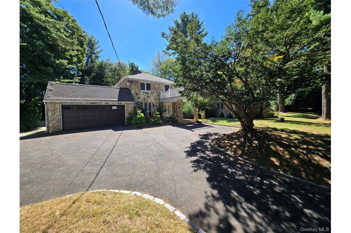 View of front of house featuring stone siding, driveway, an attached garage, and a front yard