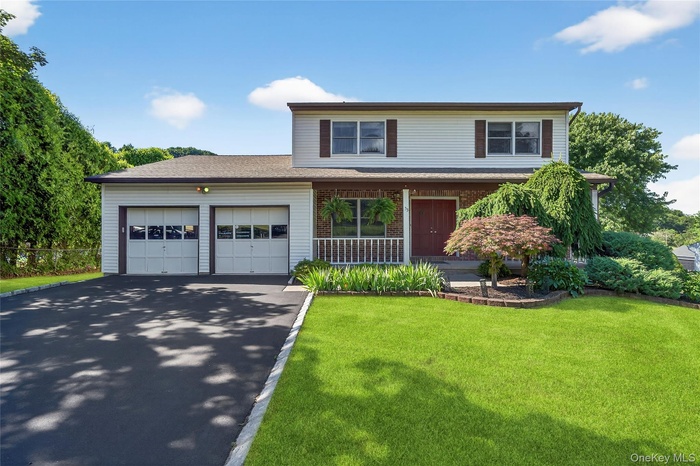 Traditional-style home featuring a garage, a porch, asphalt driveway, a front lawn, and brick siding