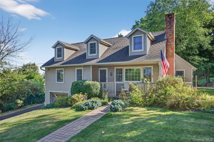 New england style home featuring a front yard, a shingled roof, and covered porch