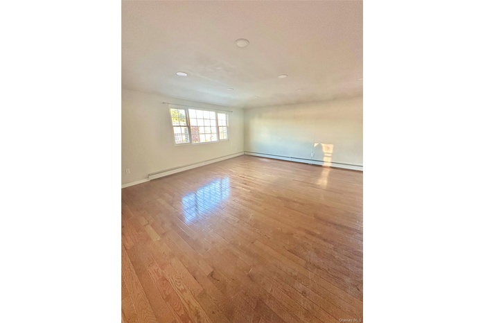 Empty room featuring light wood-style flooring, a baseboard radiator, and a textured ceiling