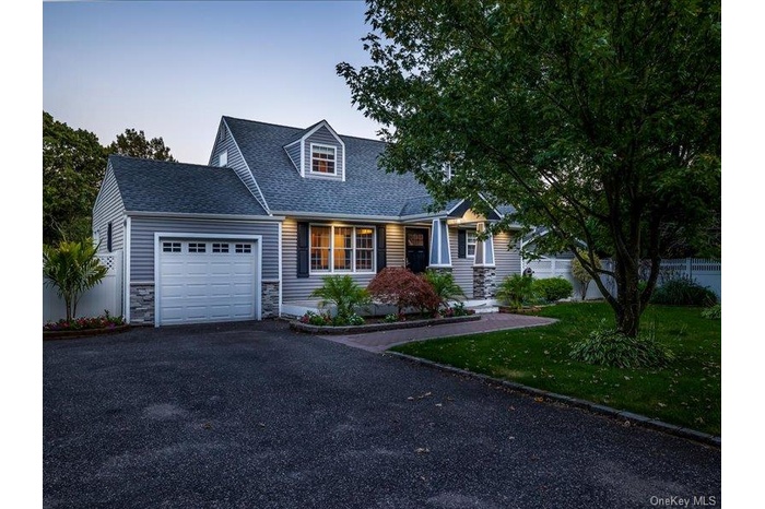 Cape cod home with roof with shingles, an attached garage, stone siding, and asphalt driveway