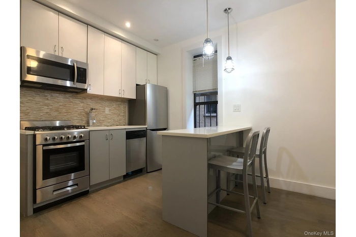 Kitchen with wood finished floors, stainless steel appliances, tasteful backsplash, a peninsula, and a kitchen bar