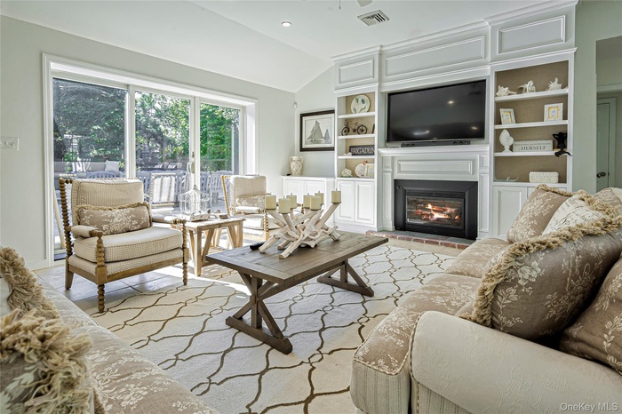 Living area with a glass covered fireplace, vaulted ceiling, recessed lighting, and built in shelves