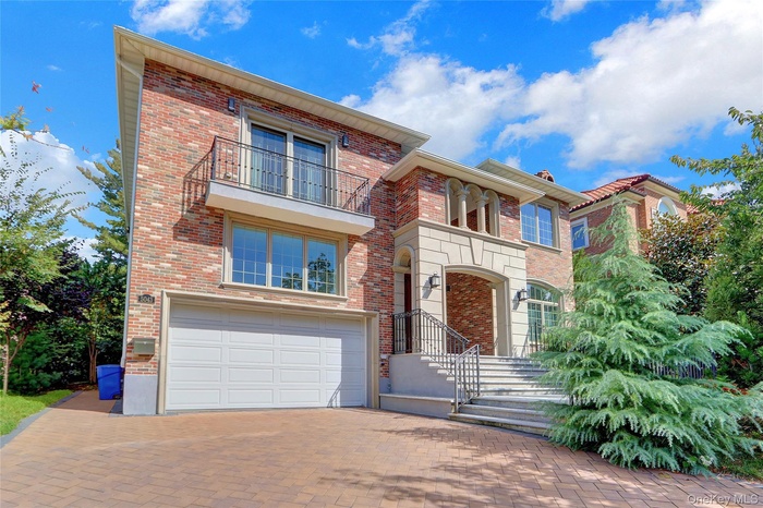 View of front of home with an attached garage, a balcony, decorative driveway, and brick siding
