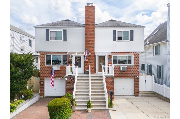 View of front facade with brick siding, a chimney, an attached garage, driveway, and stairs