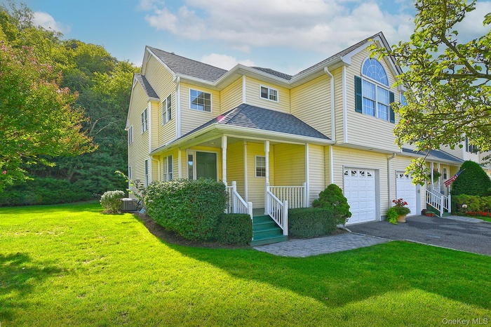 View of front of house with covered porch, an attached garage, driveway, a front yard, and a shingled roof